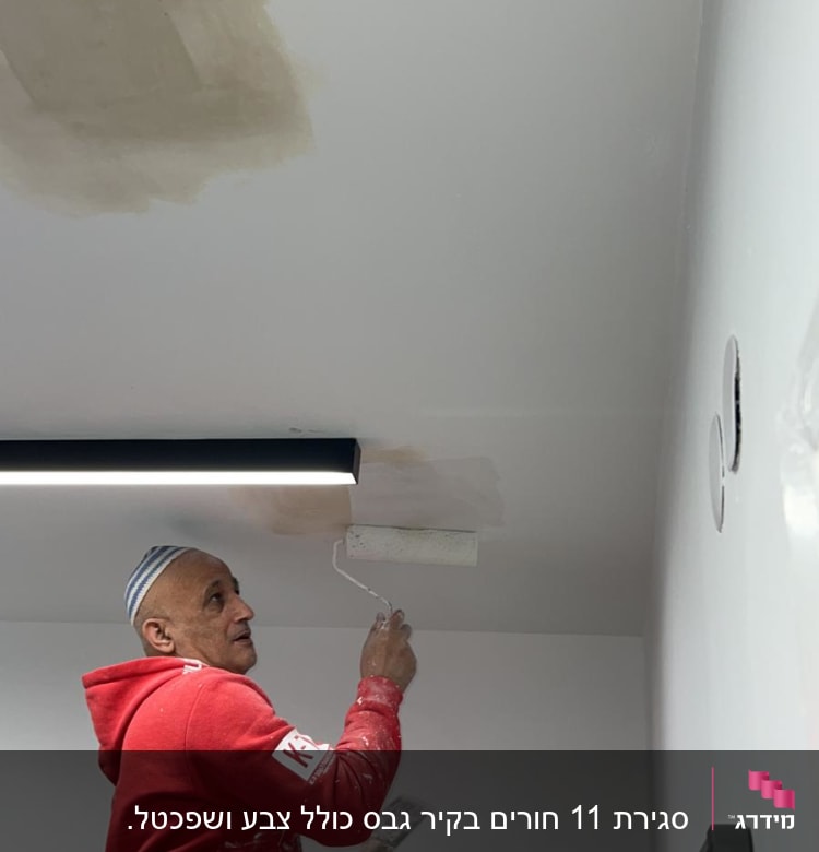 אדם צובע תקרה עם רולר וצבע לבן